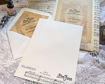 May include: A vintage-style sheet music envelope with a cream background and a black and white image of a musical score. The envelope has a title that reads "Don Juan" and "W.A. Mozart" in black text. The envelope is on a white lace surface.