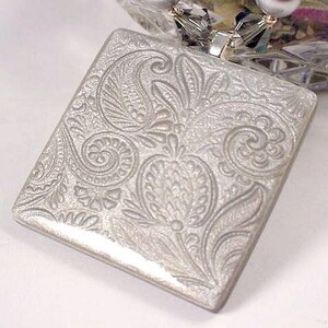 May include: A silver square pendant with an embossed paisley design.