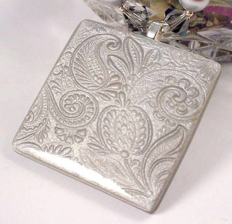 May include: A silver square pendant with an embossed paisley design.