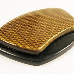 以下が含まれることがあります： 黒色の土台に載せられた、金色で質感のある長方形の物体。物体は蜂の巣のような模様をしている