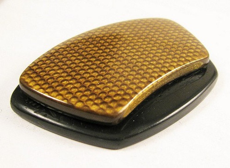 May include: A gold-colored, textured, rectangular object with a black base. The object has a honeycomb pattern.