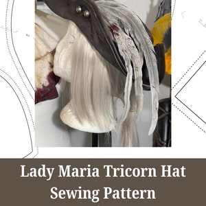 May include: A brown leather tri-corner hat with a white feather plume. The hat is decorated with two silver buttons and has a blood-splattered effect. The hat is on a white mannequin head. The image includes the text "Lady Maria Tricorn Hat Sewing Pattern" and "eufiemoon cosplay & crafting".