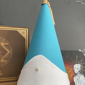May include: A turquoise party hat with a white brim and a gold tassel. The hat has a gold tip and a small gold button on the front. The hat is made of felt and fabric.