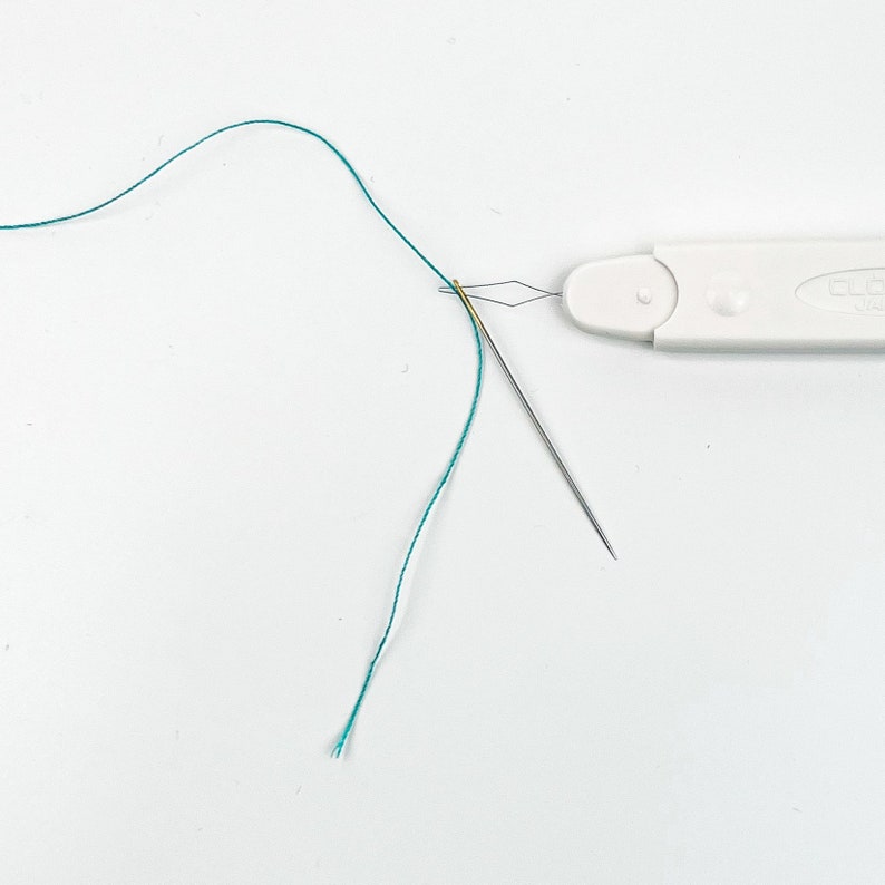 K&ouml;nnte beinhalten: Ein wei&szlig;er Plastik-Nadelf&auml;der mit einem gr&uuml;nen Faden, der durch die Nadel geht. Die Nadel ist gef&auml;delt und der Nadelf&auml;der liegt auf einer wei&szlig;en Oberfl&auml;che.