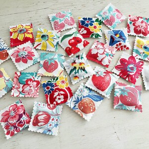 以下が含まれることがあります： 赤、黄、青、緑、白の色合いの様々な花柄とフルーツ柄が施された、小さな正方形の布製のクッションが20個あります。クッションは明るい木製の表面にランダムに配置されています。