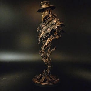 Peut inclure: Une figurine de médecin de peste de couleur bronze sur une base circulaire. Le personnage porte un chapeau à larges bords et un masque à long bec, le bas du corps se dissolvant en une forme tourbillonnante, déchiquetée et texturée.