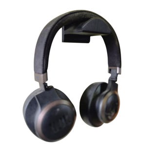 Op de afbeelding: Zwarte koptelefoon met een bruine accent op de oorschelpen hangt aan een zwarte koptelefoonstandaard.