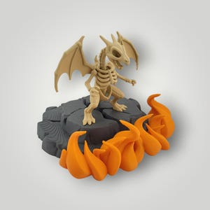 Può includere: Una statuetta di drago scheletrico beige con ali spiegate è posta su una base rocciosa grigio scuro. Fiamme arancioni brillanti si alzano dalla base. Il drago ha una struttura ossea dettagliata, creando un tema fantasy.