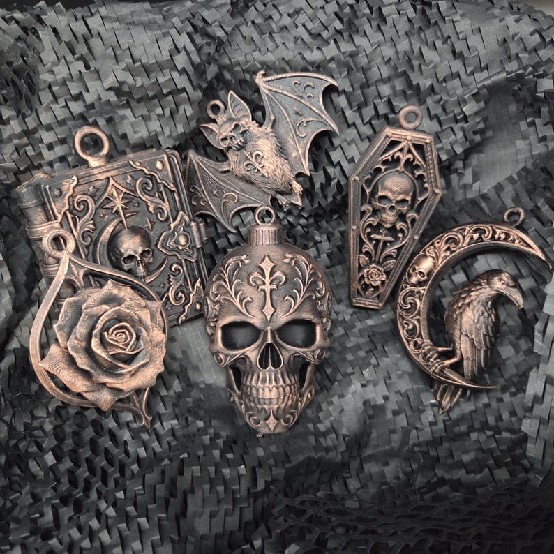May include: A collection of five copper-toned ornaments featuring a skull, a bat, a coffin with a skull, a rose, and a raven perched on a crescent moon. Each piece includes intricate embossed details and a small loop at the top for hanging.