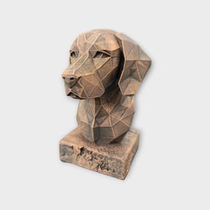 Könnte beinhalten: Bronze farbene geometrische Hundebüste. Kopf und Hals des Hundes bestehen aus miteinander verbundenen Dreiecksflächen, wodurch eine moderne Low-Poly-Ästhetik entsteht. Die Skulptur steht auf einem rechteckigen Sockel.