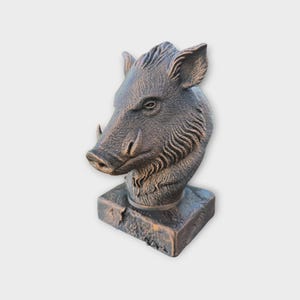 May include: A bronze-colored sculpture of a boar's head, featuring detailed fur and tusks. The sculpture is mounted on a square base, showcasing a rustic, textured finish. This decorative piece is ideal for home decor.