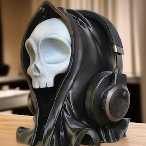 May include: A black skull wearing headphones with a black fabric draped over its head. The skull is white with a detailed face.