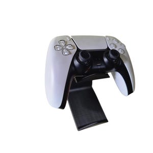 Op de afbeelding: Een witte videogamecontroller met zwarte knoppen en analoge sticks is gemonteerd op een zwarte standaard.