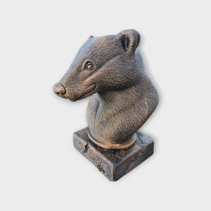 Può includere: Scultura color bronzo di una testa di cinghiale, con dettagliata texture della pelliccia e base quadrata. La testa del cinghiale è girata di lato, mostrando il muso, l'occhio e l'orecchio. La scultura ha un aspetto invecchiato.