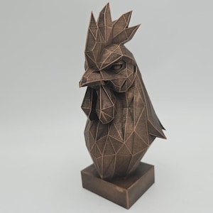 Könnte beinhalten: Eine bronzefarbene geometrische Hahnskulptur. Kopf und Hals des Hahns bestehen aus dreieckigen Facetten, was ihm ein modernes, kantiges Aussehen verleiht. Er steht auf einem quadratischen Sockel und zeigt ein detailliertes, künstlerisches Design.