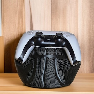 Può includere: Un controller di gioco wireless bianco con pulsanti e stick analogici neri, appoggiato su un supporto nero a forma di palla da basket.