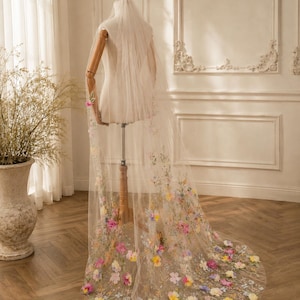 May include: A long, sheer bridal veil made of fine tulle, featuring intricate, multi-colored floral embroidery and three-dimensional fabric flower appliqués in shades of pink, yellow, blue, and purple, cascading down the length of the fabric.
