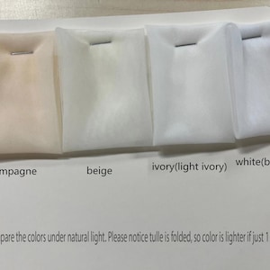 May include: A color comparison of tulle fabric samples in champagne, beige, ivory, and white. Each sample is folded and secured with a staple. Text on the card reads "Please compare the colors under natural light."