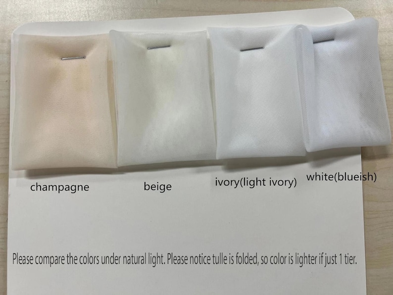 May include: A color comparison of tulle fabric samples in champagne, beige, ivory, and white. Each sample is folded and secured with a staple. Text on the card reads "Please compare the colors under natural light."