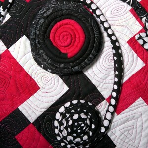 May include: A black and white fabric quilt with a red and black fabric flower design. The quilt is made of squares and has a white background with black and white polka dots.