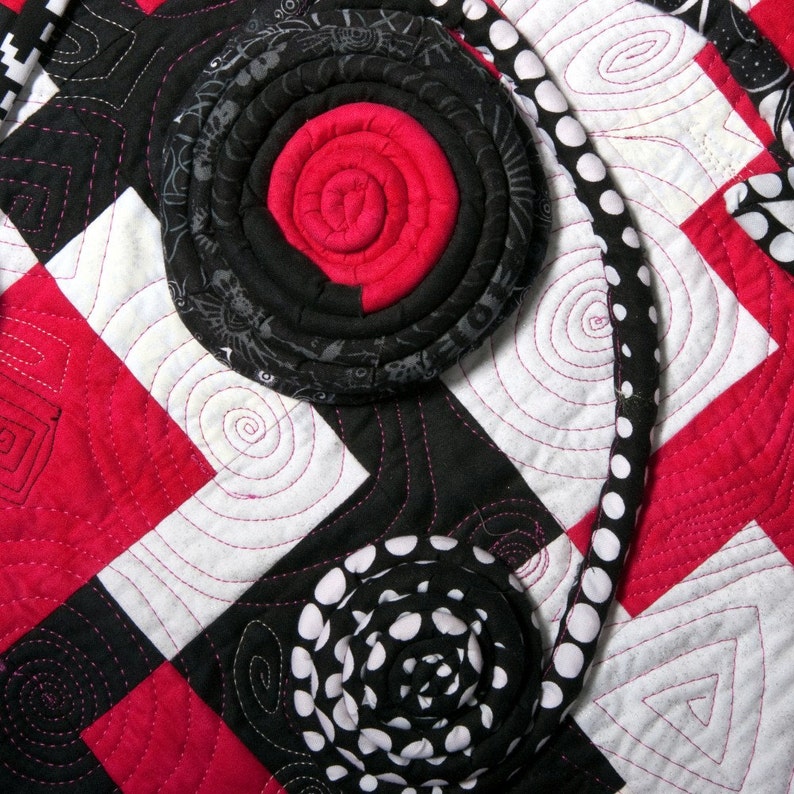 May include: A black and white fabric quilt with a red and black fabric flower design. The quilt is made of squares and has a white background with black and white polka dots.
