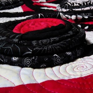 May include: A close-up of a black and white fabric quilt with a red and white center. The quilt is made of fabric scraps and has a unique, hand-stitched design.