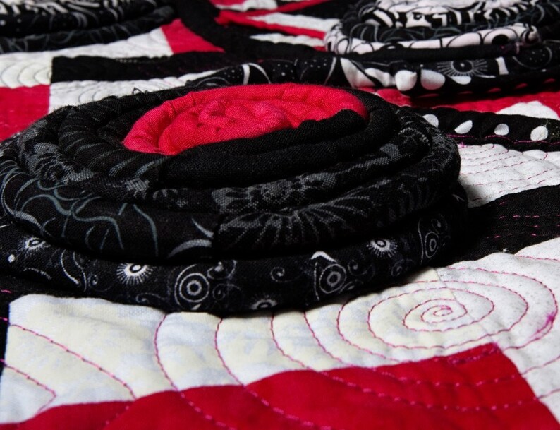 May include: A close-up of a black and white fabric quilt with a red and white center. The quilt is made of fabric scraps and has a unique, hand-stitched design.
