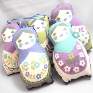 May include: Five handmade fabric doll ornaments with floral patterns. The dolls are in shades of purple, blue, green, and white. Each doll has a painted face with blue eyes and pink lips.