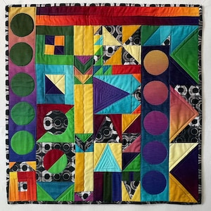 Puede incluir: Una colcha colorida con formas geométricas en tonos de rojo, naranja, amarillo, verde, azul, morado y negro. La colcha está hecha de cuadrados, triángulos y círculos.