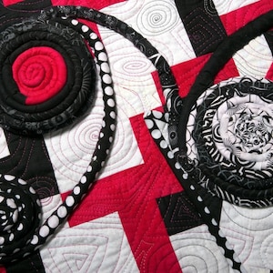 May include: A quilt with a black, white, and red color scheme. The quilt is made of fabric scraps sewn together in a patchwork design. The quilt features a variety of circular shapes and patterns.