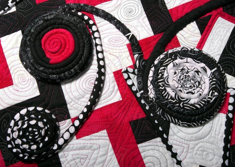 May include: A quilt with a black, white, and red color scheme. The quilt is made of fabric scraps sewn together in a patchwork design. The quilt features a variety of circular shapes and patterns.