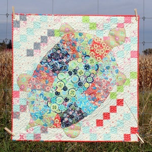 May include: A colorful patchwork quilt featuring a large, whimsical turtle design. The turtle is made up of various floral and geometric patterns in shades of blue, green, pink, and red. The quilt is bordered with a white fabric with red and gray squares.