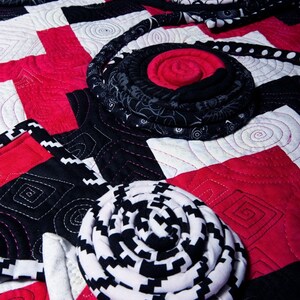 May include: A quilt with a black and white checkered pattern and red squares. The quilt is decorated with fabric rosettes in various colors and patterns.
