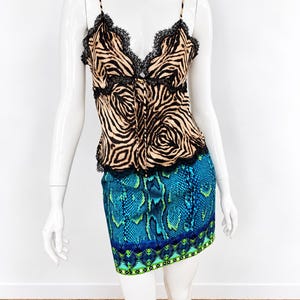 May include: A sleeveless camisole top featuring a tan and black zebra print with black lace trim along the neckline and hem, paired with a short skirt displaying a blue and green snakeskin pattern and a geometric border at the bottom.