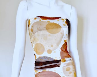 Könnte beinhalten: Ein weißes trägerloses Kleid mit einem abstrakten Druck aus Kreisen in Braun, Beige und Weiß. Das Kleid ist aus einem durchsichtigen Stoff.