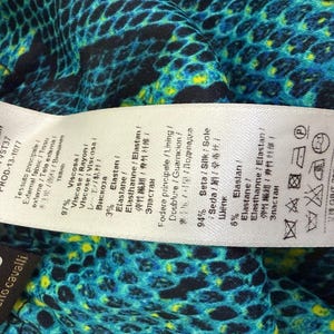 K&ouml;nnte beinhalten: Ein Roberto Cavalli Kleidungsetikett mit Stoffzusammensetzungsdetails, darunter 97% Viskose und 3% Elastan f&uuml;r das &Auml;u&szlig;ere sowie 94% Seide und 6% Elastan f&uuml;r das Futter, vor einem lebendigen blau-schwarz-gelben Schlangenmuster.