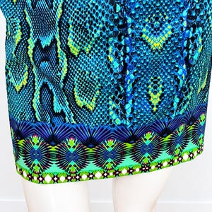 K&ouml;nnte beinhalten: Ein Rock mit einem leuchtend blauen, schwarzen und gelben Schlangenmuster auf dem Hauptteil. Der Saum ist mit einem breiten, horizontalen Band versehen, das ein symmetrisches, geometrisches Design in Lila, Gr&uuml;n und Wei&szlig; zeigt.