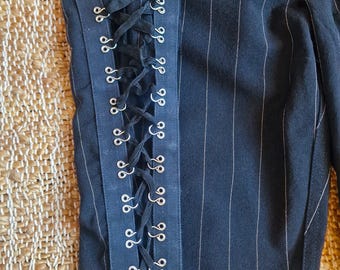 Könnte beinhalten: Schwarze Nadelstreifenhose mit einem schwarzen Band und silbernen Ösen an der Seitennaht. Das Band ist an der Seite der Hose gebunden.