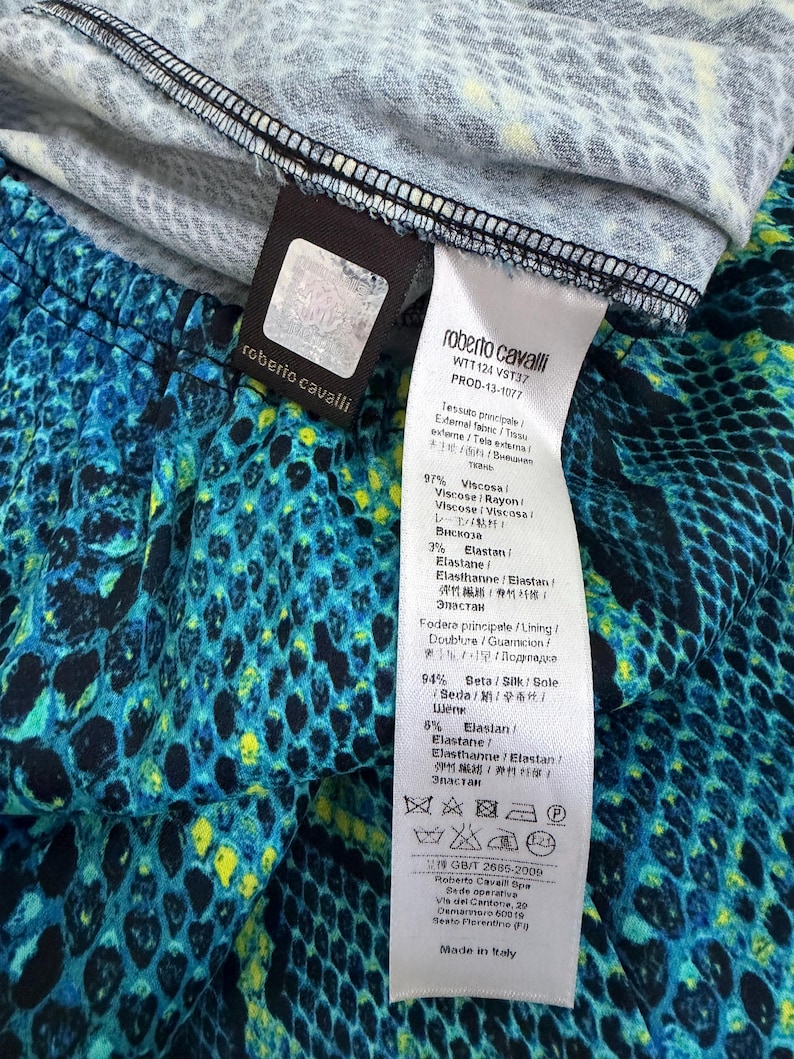 K&ouml;nnte beinhalten: Ein Roberto Cavalli Kleidungsst&uuml;ck mit einem lebendigen Schlangenmuster in Blau, Schwarz und Gelb. Das wei&szlig;e Pflegeetikett gibt 97% Viskose und 3% Elastan f&uuml;r den Au&szlig;enstoff sowie 94% Seide und 6% Elastan f&uuml;r das Futter an, inklusive Pflegesymbolen.