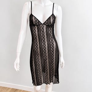 Könnte beinhalten: Ein knielanges Slip-Kleid mit schwarzem Spitzenüberzug und vertikalem Streifenmuster über einem beigen Futter. Das Kleidungsstück hat dünne Spaghettiträger, einen V-Ausschnitt und einen geraden Saum, präsentiert auf einer weißen Schaufensterpuppe.