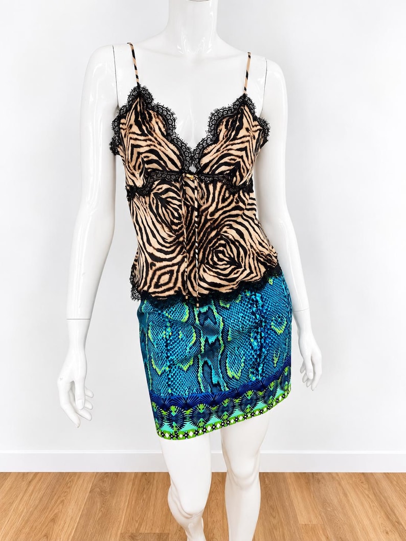 K&ouml;nnte beinhalten: Ein &auml;rmelloses Camisole-Top mit beigem und schwarzem Zebramuster und schwarzer Spitzenborte an Ausschnitt und Saum, kombiniert mit einem kurzen Rock mit blau-gr&uuml;nem Schlangenmuster und geometrischer Bord&uuml;re am Saum.