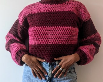 Könnte beinhalten: Ein gestreifter Häkelpullover mit langen Ärmeln in den Farben Pink und Burgunderrot.