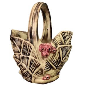 May include: Cream-colored ceramic basket with a handle and leaf-shaped sides. The basket features brown accents and pink floral details. The handle has a wood-grain appearance, and the leaves have detailed veining.