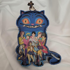 Peut inclure: Une œuvre d'art en forme de chat bleu avec une illustration détaillée d'un groupe de personnes à l'intérieur. Le chat a de grands yeux orange et un sourire sinistre. Une petite figurine d'oiseau est posée sur la tête du chat.