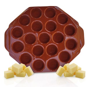 May include: A brown silicone baking mold with 20 circular cavities. The mold is filled with a light yellow substance, possibly butter or cheese, cut into cubes. The mold has a handle on each side.