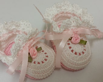 Puede incluir: Un par de botitas de bebé de crochet blanco con cinta de satén rosa y un acento de flor rosa.