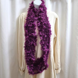May include: A purple fuzzy scarf with a long, flowing design. The scarf is made of a soft, fluffy material and is perfect for adding a touch of warmth and style to any outfit.