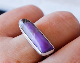 May include: A silver ring with a purple and gray gemstone set in a rectangular shape.