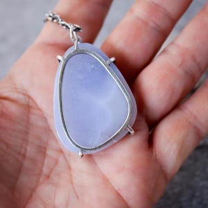 May include: A silver pendant with a light blue agate stone set in a bezel setting. The pendant is on a silver chain.