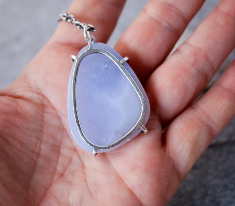 May include: A silver pendant with a light blue agate stone set in a bezel setting. The pendant is on a silver chain.